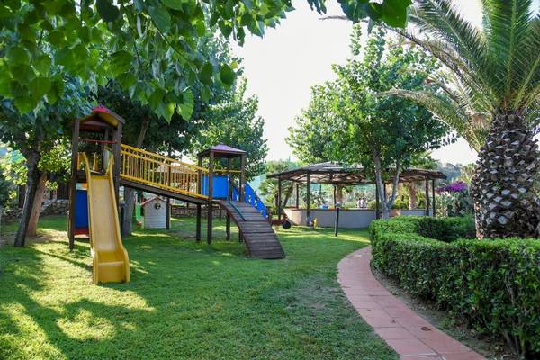 Kinderspielplatz im Baia del Sole Hotel mit Rutsche und Spielgeräten unter Bäumen.