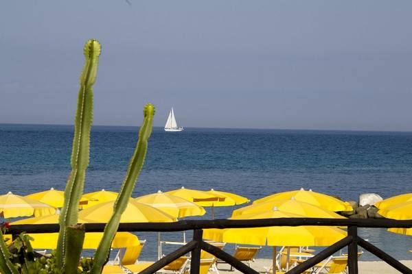 Segelboot am Horizont vor dem Baia del Sole Hotel mit gelben Sonnenschirmen am Strand