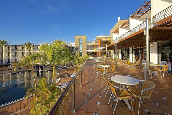 Terrasse des Mirador Papagayo by LIVVO Hotels mit Tischen und Stühlen, umgeben von Palmen und einem Swimmingpool.