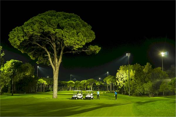 Golfplatz bei Nacht mit Beleuchtung, zwei Golfwagen und zwei Spielern