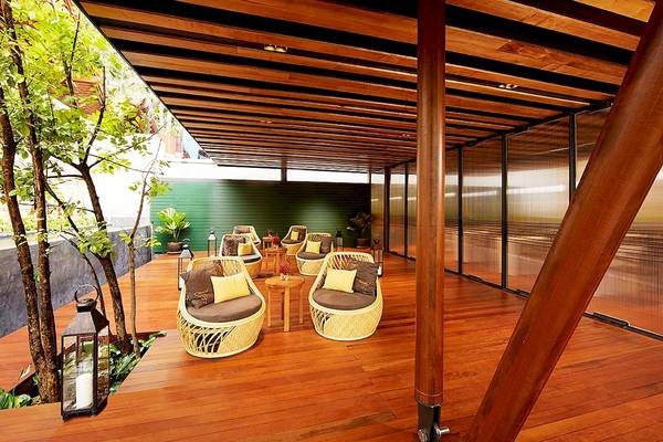 Terrasse des Tubkaak Krabi Boutique Resorts mit Holzböden, Rattanmöbeln und Pflanzen.
