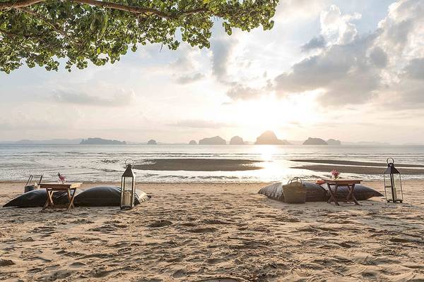 Strand des Tubkaak Krabi Boutique Resorts bei Sonnenuntergang mit Tischen, Kissen und Laternen.