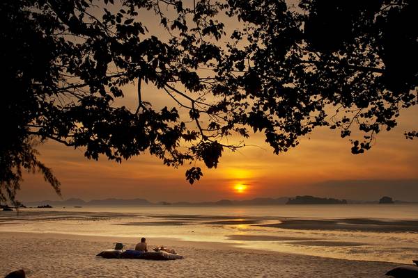 Sonnenuntergang am Strand des Tubkaak Krabi Boutique Resorts mit zwei Personen auf Kissen und Decken.
