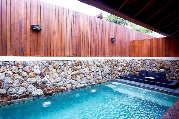 Außenpool des Tubkaak Krabi Boutique Resorts mit Steinwand und Holzzaun.