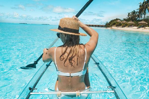 Frau im Kajak auf klarem Wasser am Strand des Reethi Faru Resorts