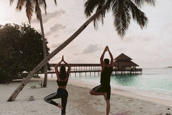 Ein Paar praktiziert Yoga auf dem Strand im Reethi Faru Resort.