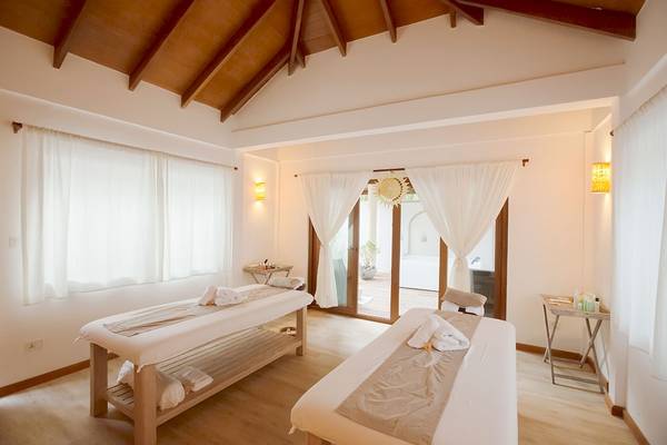 Behandlungsraum im Reethi Faru Resort mit zwei Massagetischen und weißen Vorhängen.