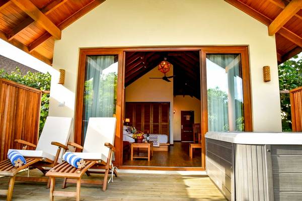 Terrasse des Reethi Faru Resorts mit Lounge-Stühlen, Whirlpool, offenem Schlafzimmer und Deckenventilator.