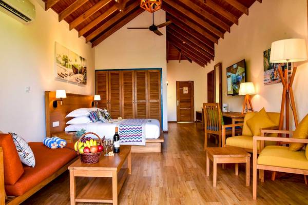 Ein Schlafzimmer im Reethi Faru Resort mit Holzboden, Bett, Tisch, Stühlen und Früchten.