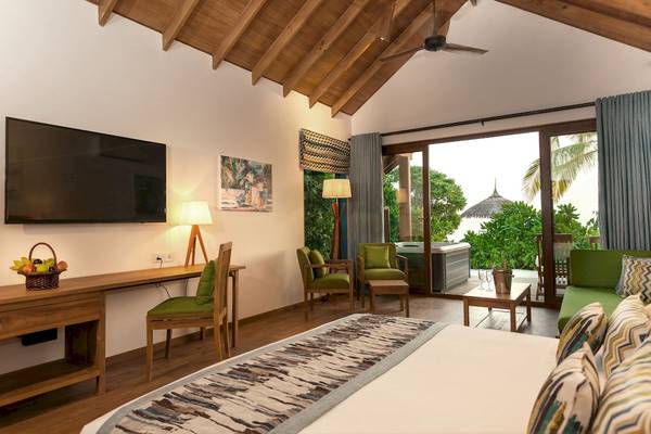 Innenansicht einer Suite im Reethi Faru Resort mit Fernseher, Schreibtisch, Stühlen und Whirlpool.