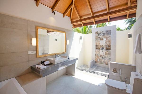 Innenansicht des Badezimmers im Reethi Faru Resort mit Badewanne, Dusche, Waschbecken und Spiegel.