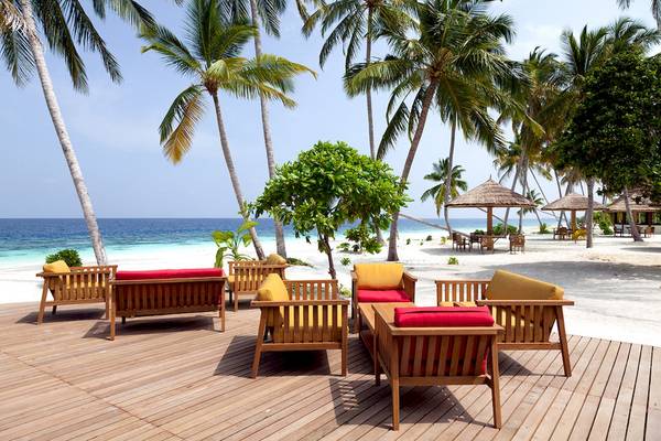 Reethi Faru Resort Strand mit Holzmöbeln und Palmen