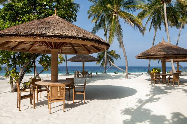Sonnensegel auf dem Strand des Reethi Faru Resorts mit Tischen und Stühlen.