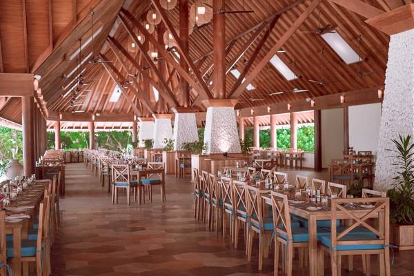 Innenansicht des Restaurants im Reethi Faru Resort mit hölzerner Struktur und Tischdecken.