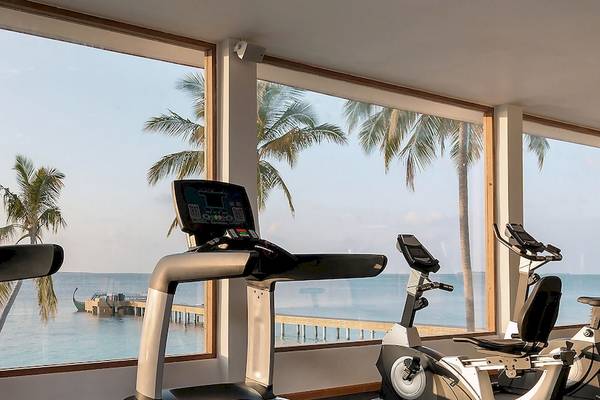 Fitnesscenter im Reethi Faru Resort mit Blick auf das Meer und Palmenbäume.