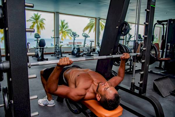 Ein Mann macht Bankdrücken im Fitnessstudio des Reethi Faru Resorts.