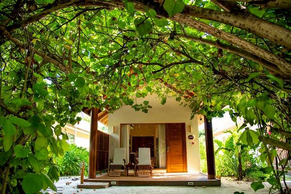 Außenansicht einer kleinen Hütte im Reethi Faru Resort mit zwei Stühlen auf der Veranda.