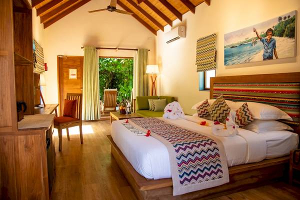 Innenansicht eines Zimmers im Reethi Faru Resort mit Bett, Sofa und Fenstern.