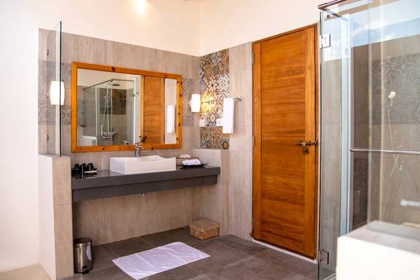 Badezimmer im Reethi Faru Resort mit Waschbecken, Spiegel und Duschbereich.