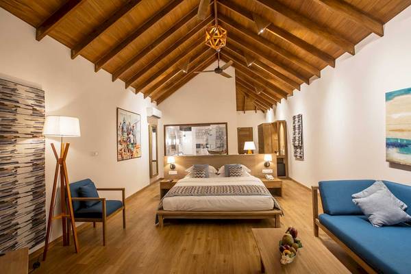 Innenansicht des Schlafzimmers im Reethi Faru Resort mit Holzboden, weißen Wänden und modernen Möbeln.