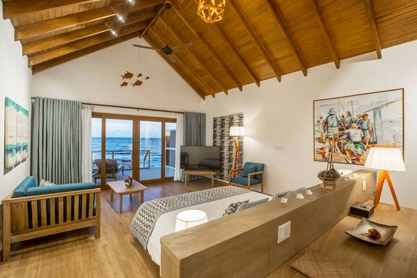 Interieur-Design eines Zimmers im Reethi Faru Resort mit Holzmöbeln, einem großen Bett und Meerblick.