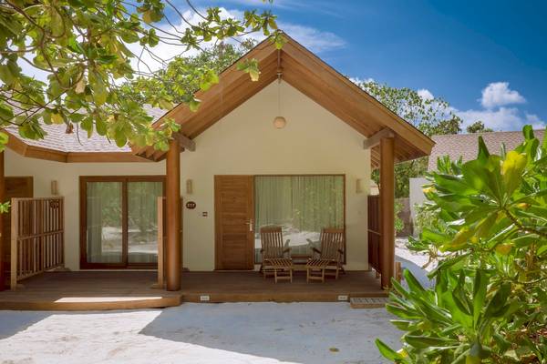 Ferienhaus des Reethi Faru Resorts mit Veranda und zwei Holzstühlen.