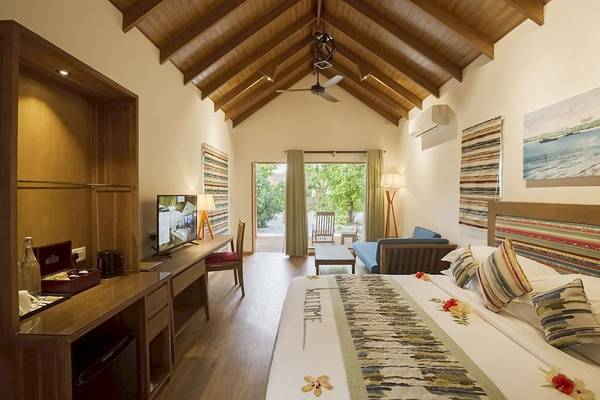 Innenansicht einer Suite im Reethi Faru Resort mit Bett, Wohnzimmer und Terrasse.