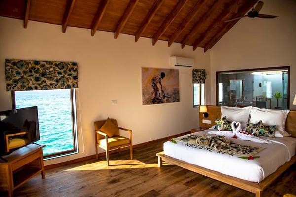 Zimmer im Reethi Faru Resort mit Meerblick, einem großen Bett, einem Fernseher und einem Stuhl.