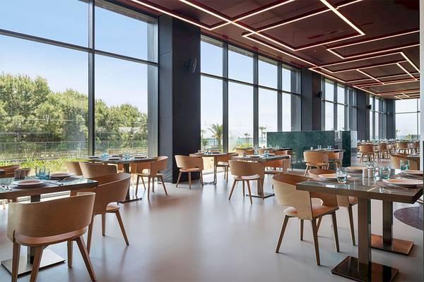 Innenansicht des Restaurants im Voyage Belek Golf & Spa mit großen Fenstern und Blick auf die Außenlandschaft.