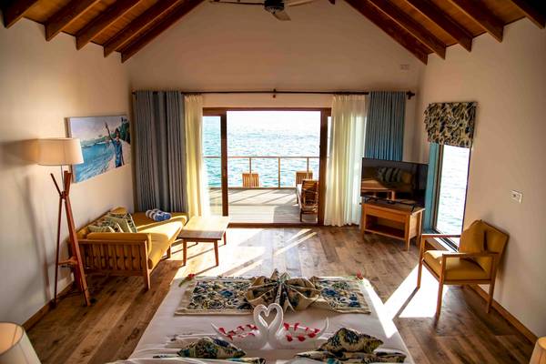 Innenansicht einer Suite im Reethi Faru Resort mit Blick auf das Meer, einem großen Bett, einem Couchtisch und einem Fernseher.