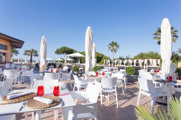 Außenbereich des Sarena de Muro Resort Mallorca mit weißen Tischen und Stühlen unter Schirmen.