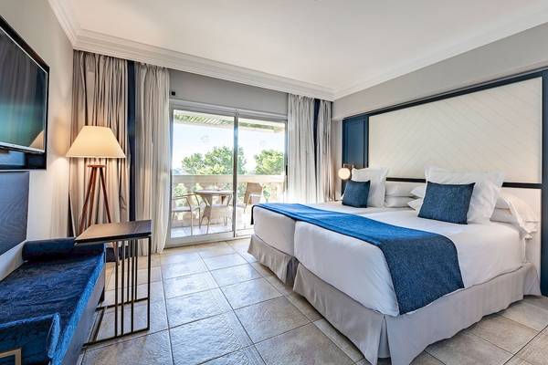 Hotelzimmer im Sarena de Muro Resort Mallorca mit Balkon, zwei Betten, Fernseher und Lampe.