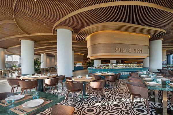 Innenansicht des Restaurants im Voyage Belek Golf & Spa Hotel mit Holzdecken, runden Tischen und Stühlen.