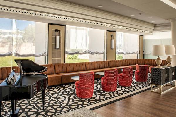 Hotellobby des Sarena de Muro Resorts auf Mallorca mit Klavier, roten Stühlen und großem Fenster.