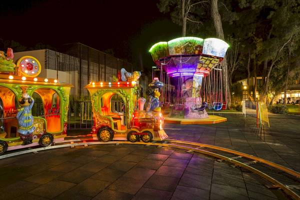 Nachtansicht einer bunt beleuchteten Achterbahn und eines Karussells im Freizeitpark.