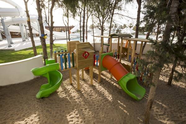 Kinderspielplatz im Voyage Sorgun Hotel mit Rutschen und Spielgeräten, umgeben von Bäumen.
