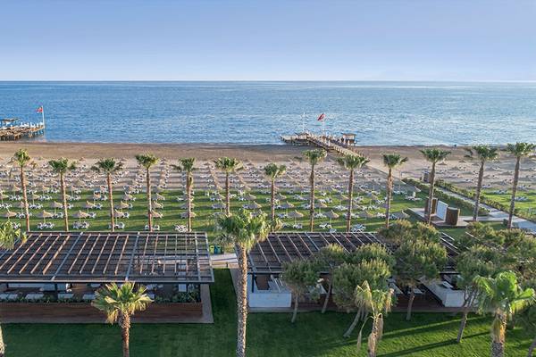 Luftaufnahme des Voyage Belek Golf & Spa Hotels mit Blick auf den Strand, Palmen und das Meer.