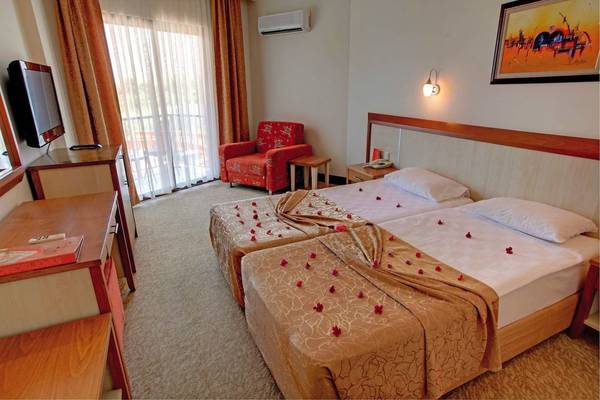 Doppelzimmer im Victory Resort mit zwei Betten, Blumenblättern, Fernseher, rotem Sessel und Lampe.