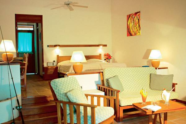 Hotelzimmer im Capitan Suizo Beachfront Boutique Hotel mit Bett, Sofa, Lampen und Tisch mit Getränken.