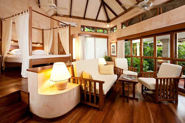 Innenansicht eines Hotelzimmers im Capitan Suizo Beachfront Boutique Hotel mit einem großen Bett, einem Sofa und Sesseln.