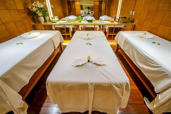 Massage-Behandlungsraum im Seaview Patong Hotel mit drei weißen Massagebetten und Blumendekoration.