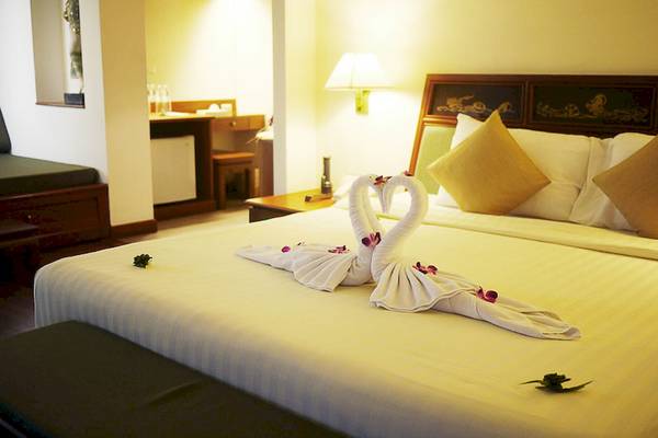 Bett im Seaview Patong Hotel mit zwei weißen Handtüchern, die in Form eines Herzens gebunden sind, und Blumen darauf.