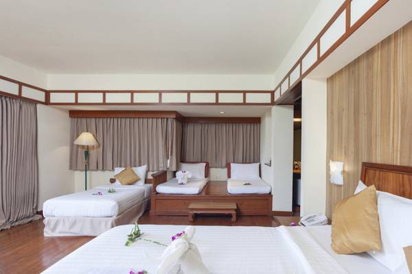 Innenansicht eines Hotelzimmers von Seaview Patong mit drei Betten, Holzmöbeln und Blumendekor.