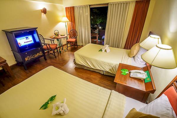 Innenansicht eines Zimmers im Seaview Patong Hotel mit zwei Betten, Tisch, Stühlen und Fernseher.