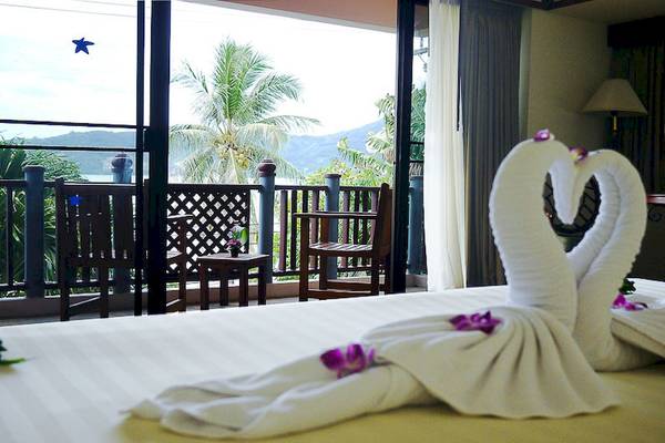 Schlafzimmer mit Blick auf den Balkon im Seaview Patong Hotel, mit zwei kunstvoll gefalteten Handtüchern in Herzform auf dem Bett.