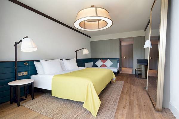 Das Schlafzimmer im Voyage Belek Golf & Spa Hotel mit einem großen Bett, einem gelben Bettlaken, Nachttischen, Lampen und einem Spiegel.