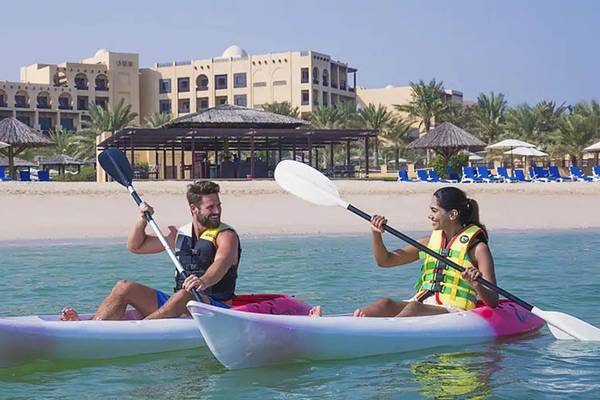 Zwei Personen auf Kajaks vor dem Hilton Ras Al Khaimah Beach Resort am Strand.