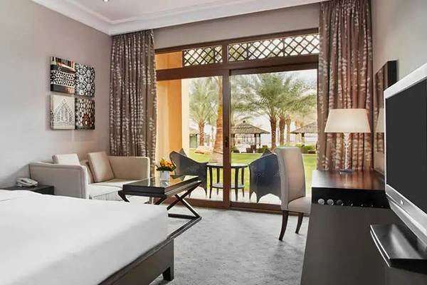 Innenansicht eines Hotelzimmers im Hilton Ras Al Khaimah Beach Resort mit Bett, Wohnzimmerbereich und Terrasse.