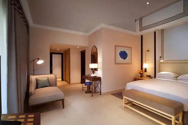 Innenansicht eines Schlafzimmers im Hilton Ras Al Khaimah Beach Resort mit einem großen Bett, Nachttischen, Sesseln und Dekorationsgegenständen.