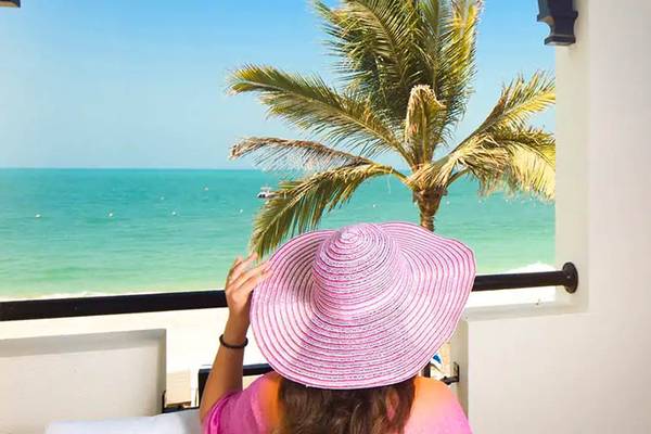 Frau mit Hut auf dem Balkon des Hilton Ras Al Khaimah Beach Resort mit Meerblick.